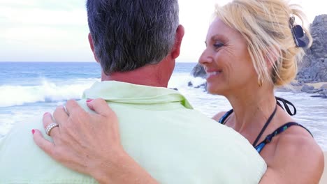 An-older-woman-smiling-and-whispering-"I-love-you"-into-her-husband's-ear-at-the-beach