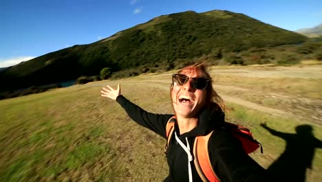 Young-female-hiking-takes-selfie-portrait-with-mountains-on-background