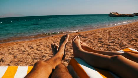 Piernas-de-pareja-sin-gente-tirada-en-Beach-Sun-Lounger-cerca-del-Mar-Rojo