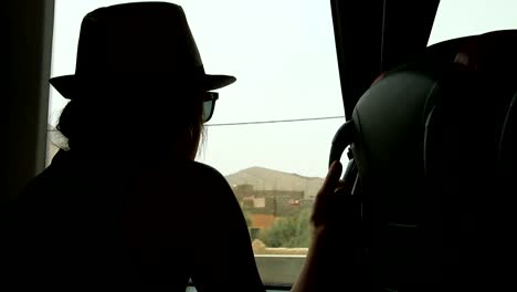 Young-woman-looking-trough-the-window-and-playing-with-hands-sitting-on-backseats-in-bus-during-road-trip