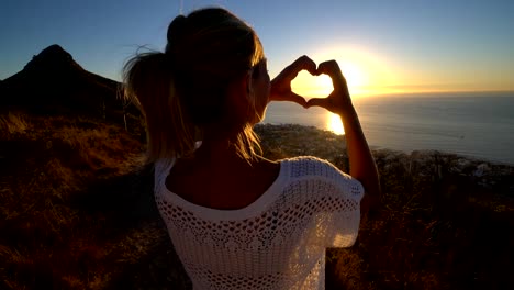 Joven-viendo-la-puesta-de-sol-junto-al-mar,-hace-que-la-forma-del-corazón