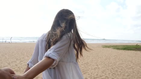 Girl-holding-male-hand-and-running-on-tropical-exotic-beach-to-the-ocean.-Follow-me-shot-of-young-woman-pull-her-boyfriend-on-the-sea-shore.-Summer-vacation-or-holiday.-Point-of-view-POV