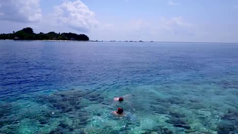 v04065-Aerial-flying-drone-view-of-Maldives-white-sandy-beach-2-people-young-couple-man-woman-snorkeling-swimming-diving-on-sunny-tropical-paradise-island-with-aqua-blue-sky-sea-water-ocean-4k