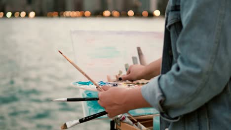 Close-up-view-of-young-woman-holding-the-brushes-and-drawing-the-picture-on-shore-of-Michigan-lake,-Chicago,-America