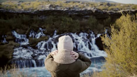 Vista-posterior-de-la-mujer-joven-de-pie-en-el-valle-de-la-montaña-y-mirando-en-cascadas-de-Islandia,-explorar-la-naturaleza