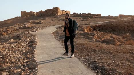 Casual-European-tourist-walks-to-ancient-ruins.-Relaxed-man-on-summer-desert-road-takes-a-smartphone-photo.-Israel-4K