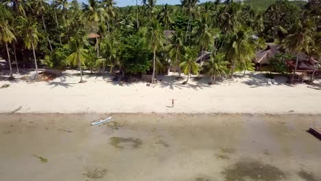 Drone-shot-aerial-view-of-young-man-arms-outstretched-relaxing-on-tropical-beach,-contemplating-nature.-4K-resolution-video-shot-in-the-Philippines,-Asia.-People-travel-vacations-concept