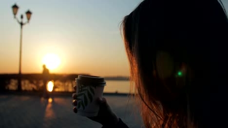 Mädchen-hält-Tasse-mit-Kaffee-und-schlürfen,-erstaunlichen-roten-Sonnenuntergang-über-Fluss-bewundern