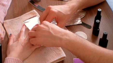 Removing-gel-Polish-from-nails.-Man-pours-remove-liquid-on-a-cotton-pad,-puts-it-on-a-woman's-nail-and-wraps-the-foil.-Close-up-hands.-High-speed.