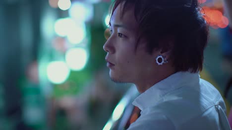 Porträt-der-schöne-japanische-Alternative-Mann-mit-Piercing.-Im-Hintergrund-Plakate-Großstadt-Werbung-Lichter-leuchten-in-der-Nacht.