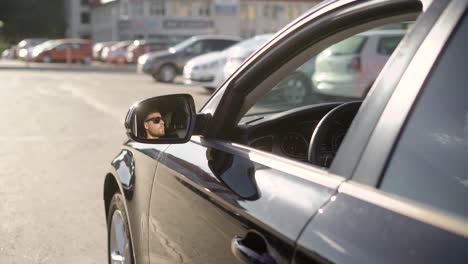 man-is-driving-big-car-on-city-roads,-view-from-outside,-his-face-is-reflecting-in-a-rearview-mirror-in-sunny-day