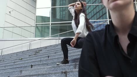 Mujer-sentada-a-otra-mujer-bailando-sobre-los-pasos-de-entrada-del-edificio-corporativo