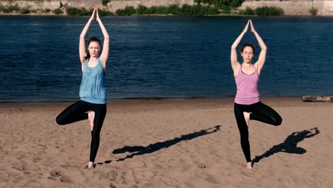 Zwei-Frau-stretching-Yoga-stehen-am-Strand-am-Fluss-in-der-Stadt.-Blick-auf-die-schöne-Stadt.-Balance-Pose.