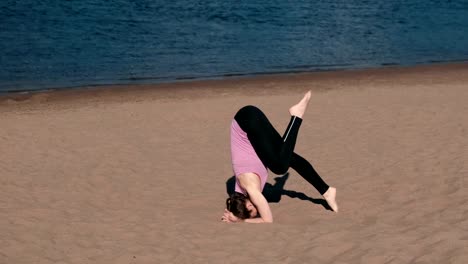 Woman-doing-yoga-on-the-beach-by-the-river-in-the-city.-Beautiful-view.-Handstand.-Twine-in-the-air.