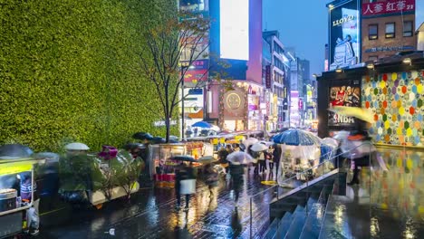 Timelapse-at-Myeong-dong-Market.People-walking-with-umbrellas-on-a-rainy-day-at-shopping-street-at-night,-Seoul,-South-Korea