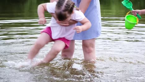 Madre-de-la-niña-lava-sus-pies-en-el-río.-Mujer-jugando-con-su-bebé-en-la-playa