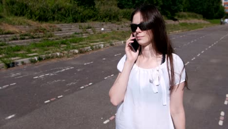 Young-brunette-girl-walking-in-the-stadium,-dials-a-number-on-mobile-phone-and-waiting-for-an-answer.