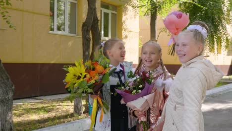 Verspielten-Schulmädchen-mit-Blumensträußen-lachen-und-Stand-in-der-Nähe-der-Schule