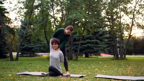 Schlankes-Girl-Yoga-Lehrer-trägt-dazu-bei,-dass-ihr-Schüler-Gomukhasana-beim-individuellen-Training-im-Park-im-Herbst-zu-verwalten.-Konzept,-Beratung,-Sport-und-Natur.