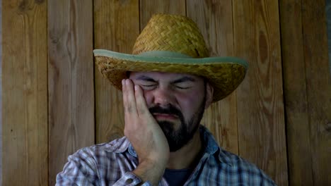 Unshaven-man-in-a-straw-hat-suffers-from-toothache