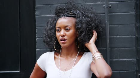 Fashionable-young-black-woman-leaning-against-a-wall-in-the-street-playing-with-her-hair,-close-up