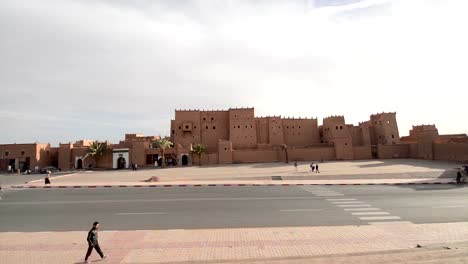 People-walking-and-cars-passing-by-in-front-of-the-outer-walls-of-the-front-façade-of-Kasbah-Taourirt