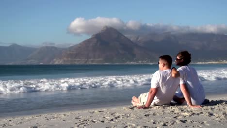 Couple-sitting-close-together-on-beach-and-enjoying-the-view,South-Africa