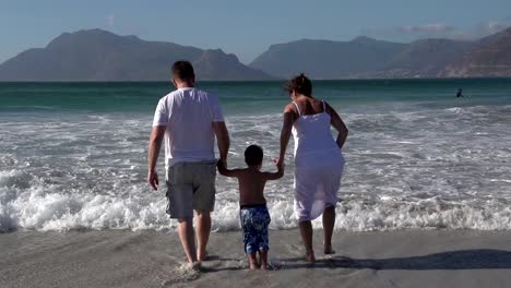 Slow-motion-of-couple-swinging-child-through-waves,-South-Africa