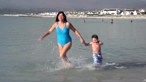 Joven-madre-y-niño-corriendo-hacia-la-cámara-en-la-playa,-Cape-Town