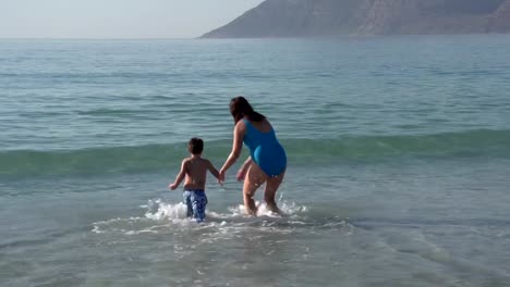 Mutter-und-junge-Jungen-spielen-im-seichten-Wasser-am-Strand,-Cape-Town