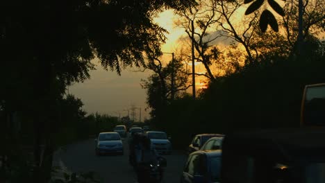 Locked-on-shot-of-traffic-moving-on-road-at-sunset,-Delhi,-India