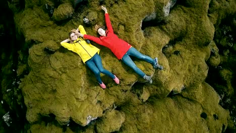 Top-aerial-view-of-two-woman-lying-on-lava-field-in-Iceland-and-rest-after-hiking.-Copter-turning-around-happy-females