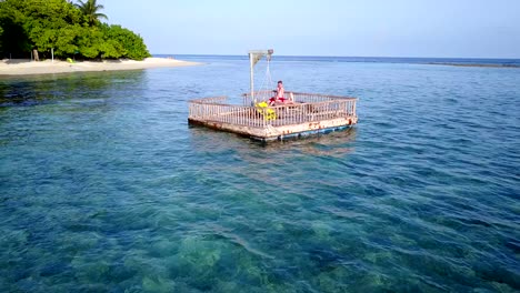 v03849-vuelo-drone-vista-aérea-de-Maldivas-playa-2-personas-pareja-hombre-mujer-relajante-en-la-isla-de-paraíso-tropical-soleado-con-cielo-azul-aqua-agua-mar-4k-flotante-pontoon-embarcadero-el-sol-juntos