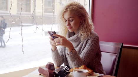 Joven-mujer-rizada-sentado-en-la-cafetería-con-teléfono