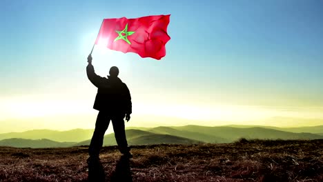 Ganador-de-hombre-exitoso-silueta-ondeando-la-bandera-de-Marruecos-en-la-parte-superior-del-pico-de-la-montaña,-fondo-Cinemagraph-lazo