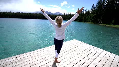 Young-woman-arms-outstretched-on-lake-pier,-Canada