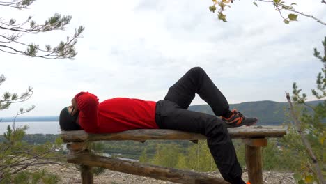 Tourist-man-He-is-lying-on-the-bench-in-the-mountains,-and-talking-on-the-phone-.--hiking.-a-tour-of-the-forest.-camping.-leisure.-ecotourism.-wild.-adventure-begins