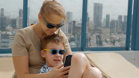 Mom-and-child-using-mobile-when-relaxing-on-hotel-rooftop-in-Tel-Aviv,-Israel