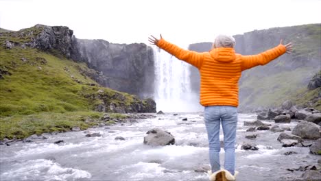 Young-woman-arms-outstretched-in-front-of-the-magnificent-waterfall-in-Iceland.-People-travel-exploration-concept--Slow-motion