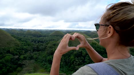 Girl-traveling-makes-heart-on-Chocolate-Hills-of-Bohol,-Philippines