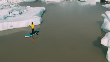 Joven-aventurero-infantil-stand-Junta-de-pádel-a-través-de-icebergs-en-el-lago-glaciar-en-Islandia