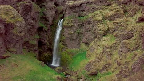 Drone-aerial-view-of-Young-woman-arms-outstretched-at-spectacular-waterfall-in-Iceland--4K-video