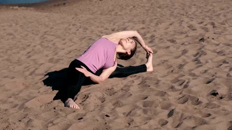 Woman-stretching-yoga-on-the-beach-in-the-city.-Sirsasana,-Supta-upavistha-konasana-pose.