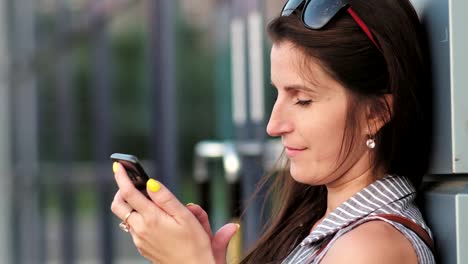 Woman-communication-or-chatting-with-somebody-using-smartphone-standing-near-glass-modern-building