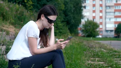 Mujer-tipos-de-un-mensaje-en-el-teléfono-sentado-en-el-parque.