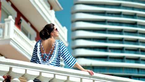 Mujer-en-gafas-de-sol-disfrutando-de-vacaciones-en-día-de-verano-en-el-balcón-poner-mano-en-el-pasamano-de-la-antigüedad