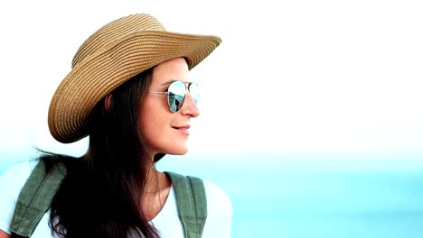 Portrait-of-pensive-young-woman-in-sunglasses-and-hat-with-backpack-enjoying-amazing-seascape