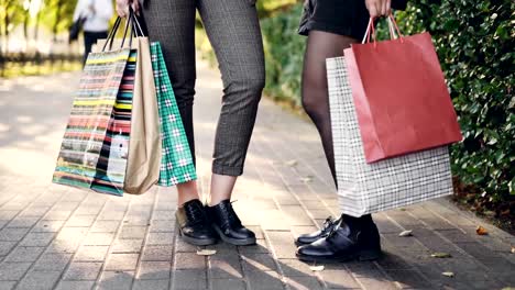 Low-angle-shot-of-female-legs-standing-on-sidewalk-holding-shopping-bags-after-happy-busy-day-in-shops-and-malls.-People,-consumerism-and-leisure-concept.