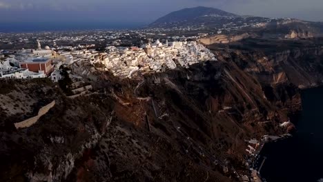 Flight-over-of-Fira-(Thira)-town-at-sunset,-Santorini-island,-Greece