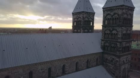 Drone-aéreo-Catedral-de-Lund-tiro.-Vuelo-siguiente-al-edificio-de-la-iglesia-y-Torres,-horizonte-de-la-ciudad-de-Lund-en-puesta-del-sol